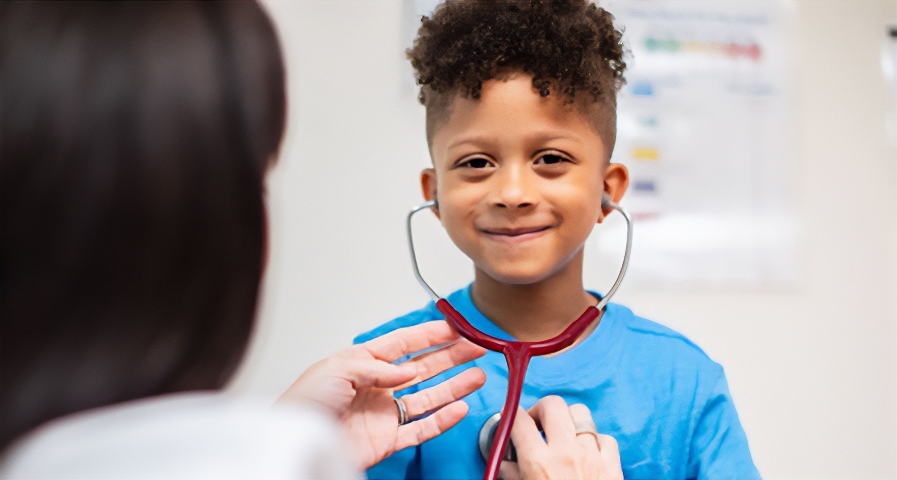 A doctor helps a cheerful young boy wearing a stethoscope listen to his heartbeat.
