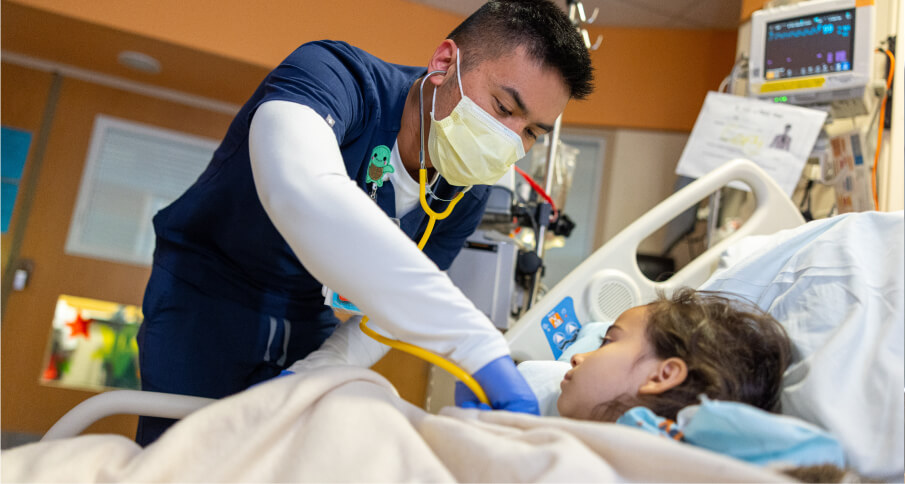A doctor helps a cheerful young boy wearing a stethoscope listen to his heartbeat.