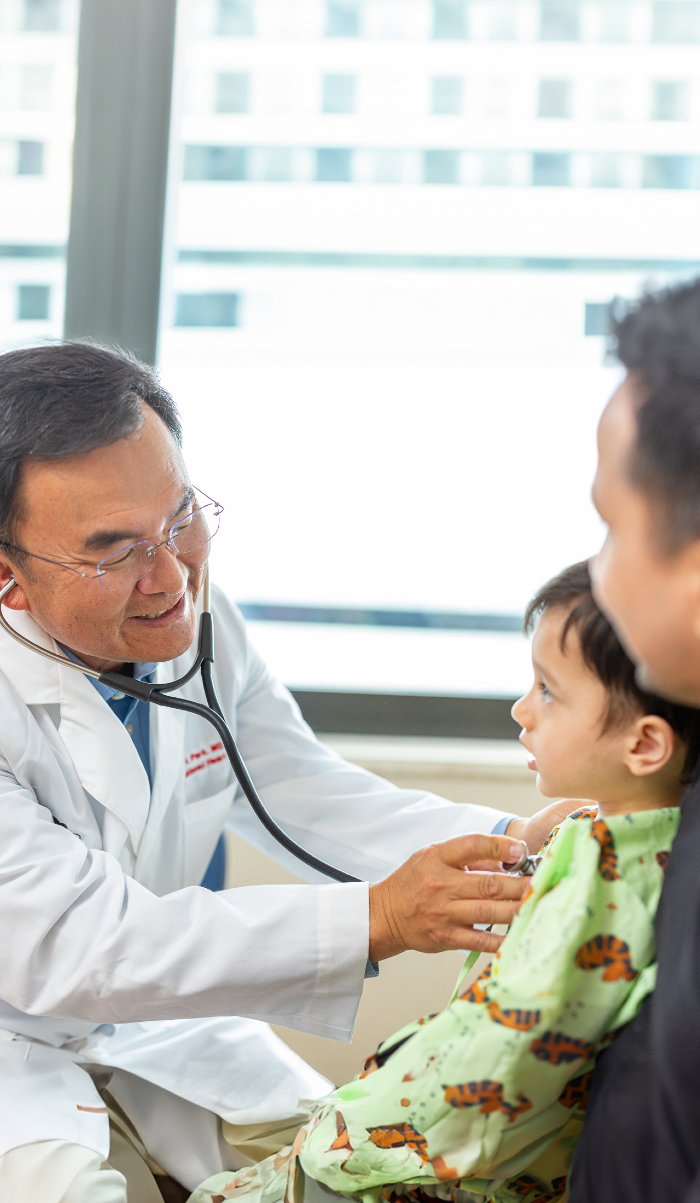 Doctor using stethoscope to check childs heartbeat while sitting by the parent.